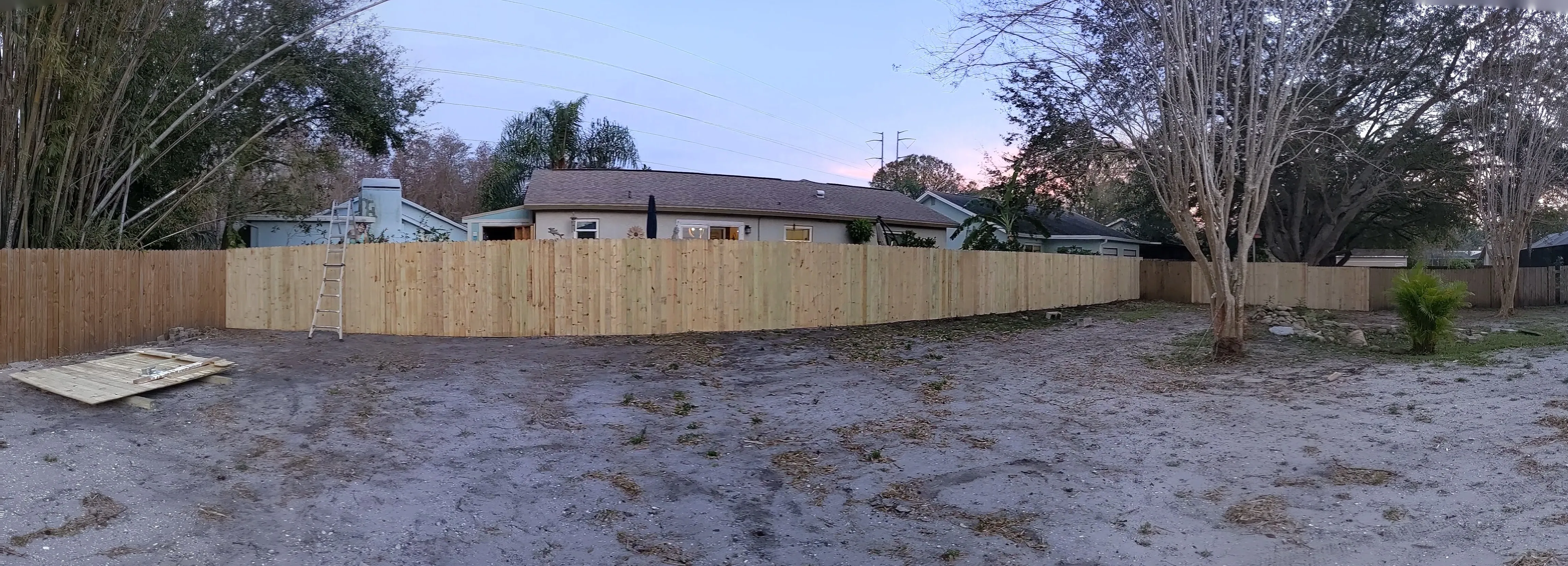Long L-shaped run of new pressure-treated wood privacy fence with dog-ear pickets enclosing a large Tampa Bay backyard